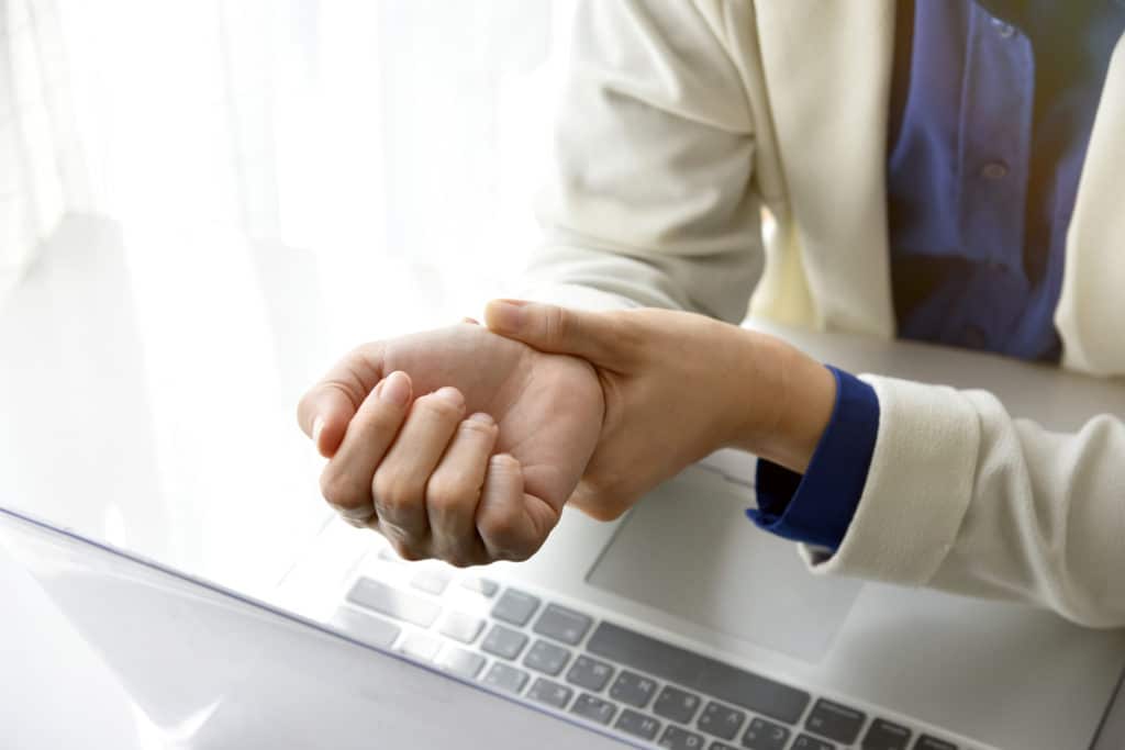 Professional holding their wrist in pain while seated at a laptop, suggesting a repetitive stress or workplace injury