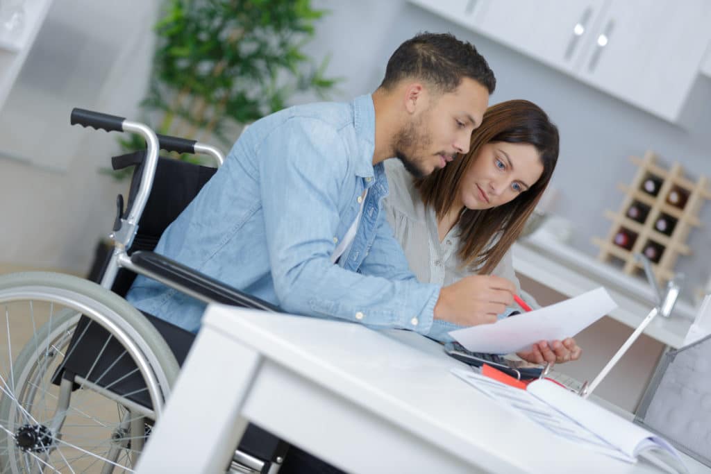Man in wheelchair reviewing legal documents with a woman at a desk, discussing disability claim paperwork together