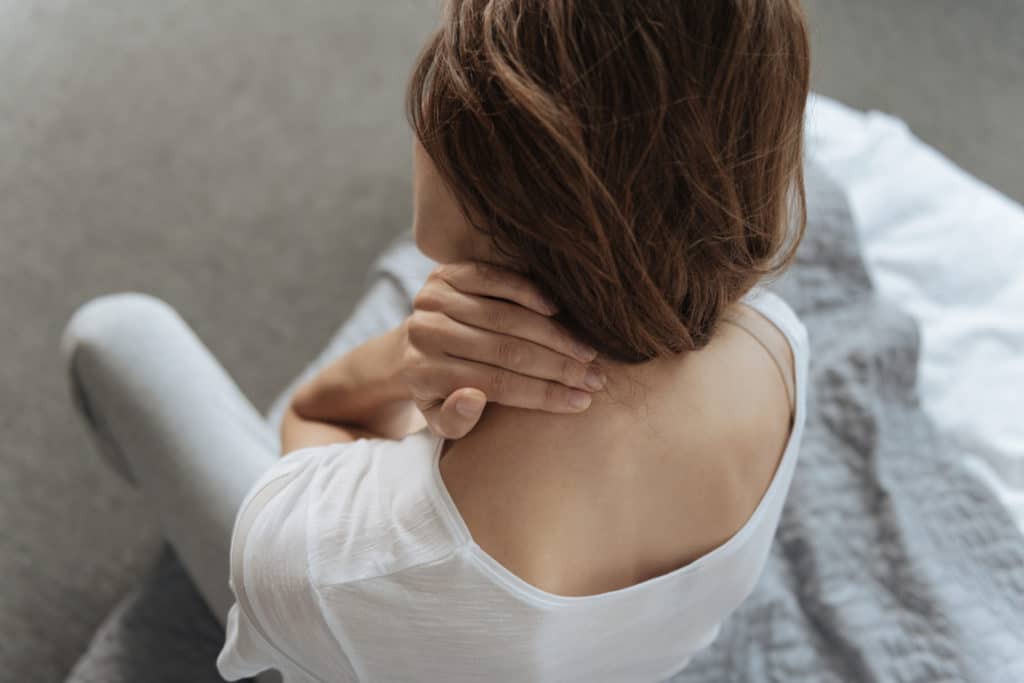 Woman in white shirt holding her neck and shoulder in pain while sitting, depicting personal injury symptoms