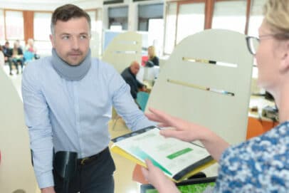 Man wearing neck brace and arm sling receiving documents from a receptionist in an office setting