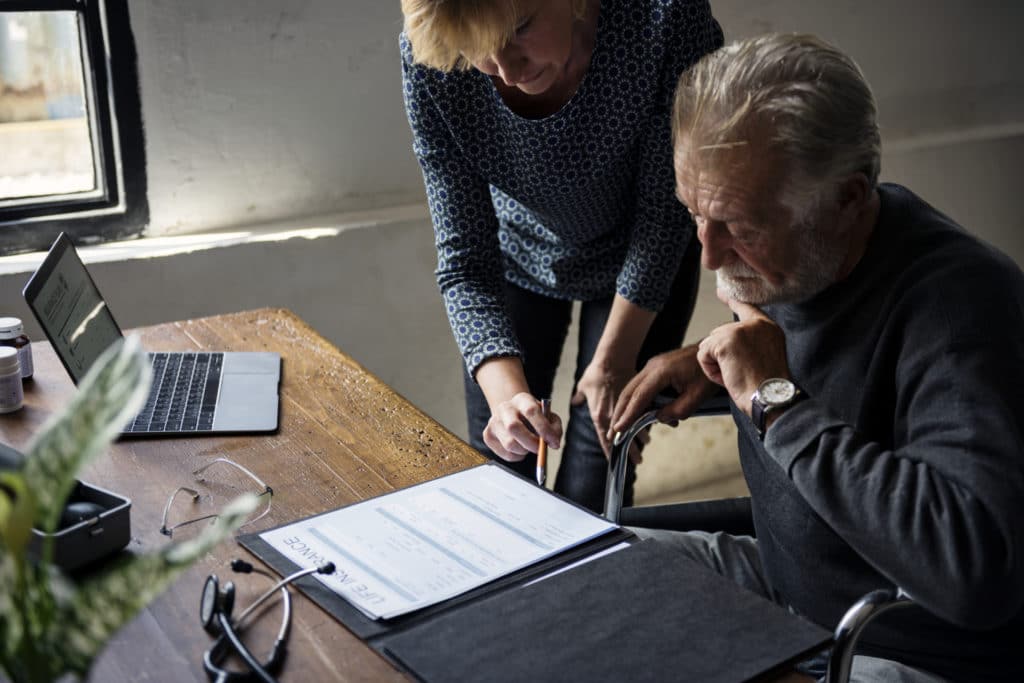 Attorney and senior client reviewing a life insurance document together at a desk with a laptop nearby