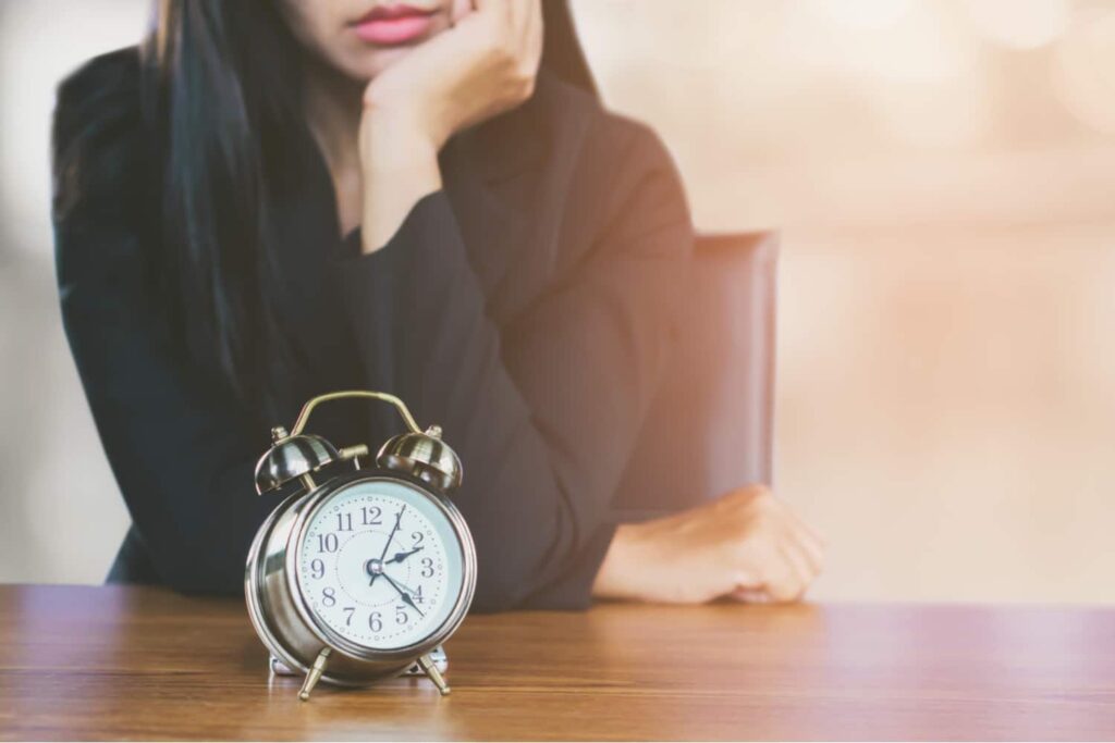 Woman in black jacket sitting at desk, resting chin on hand while staring at a vintage alarm clock, representing legal deadlines