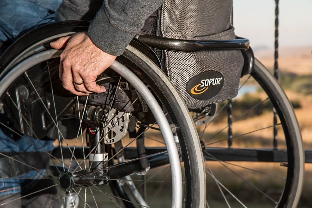 Close-up of a person's hand gripping a manual wheelchair wheel outdoors, representing disability and mobility challenges