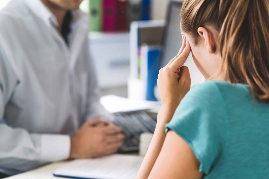 Distressed woman holding her head during a consultation with a professional at an office desk