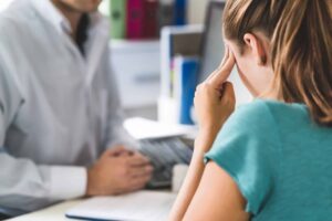 Distressed woman holding her head during a consultation with a professional at an office desk