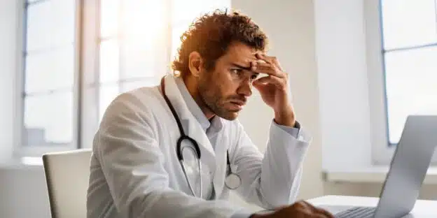 The Physician's Guide to Long-Term Disability Insurance Claims 1 Stressed physician reviewing physician disability insurance claim documents on a laptop